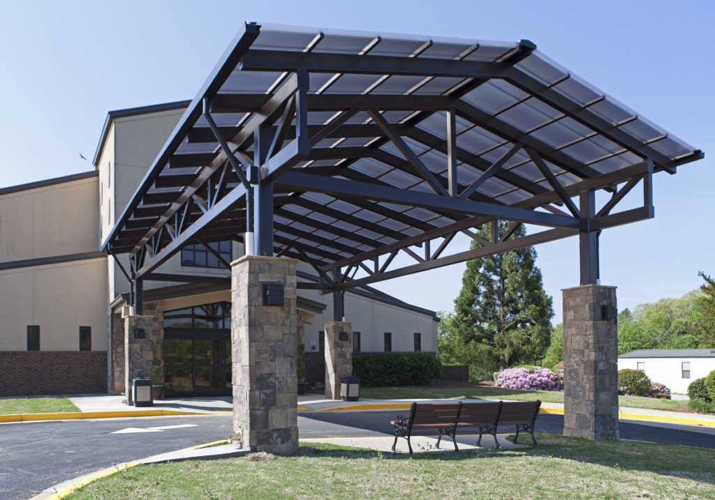 Standing Seam Skin System Canopy, 25’5” x 42’6”, 2.5/12 pitch. Glazing: 20mm Bronze Cellular Polycarbonate mounted to steel purlins, structure by others. Includes gutters and downspouts. Finish: Dark Bronze Anodized.