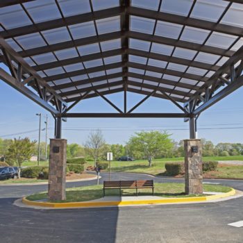 Standing Seam Skin System Canopy, 25’5” x 42’6”, 2.5/12 pitch. Glazing: 20mm Bronze Cellular Polycarbonate mounted to steel purlins, structure by others. Includes gutters and downspouts. Finish: Dark Bronze Anodized.